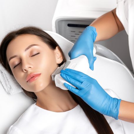 Mujer recibiendo tratamiento facial con guantes azules y toalla.